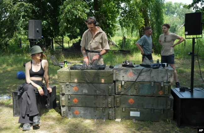 A DJ holds a techno performance while young volunteers clear debris from a building destroyed by a Russian rocket in the village of Yahidne, Chernihiv Region, Ukraine, Sunday, July 24, 2022