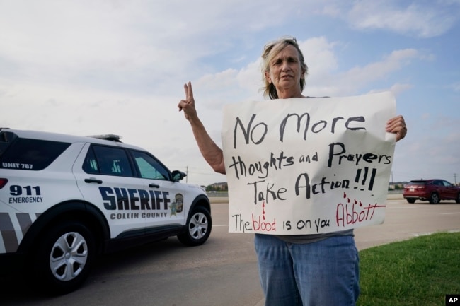 Mary Ann Foley holds a protest sign outside a prayer vigil following a mass shooting the day before, May 7, 2023, in Allen, Texas.