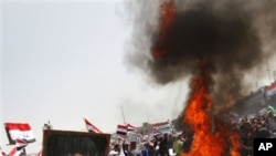 Followers of radical Shi'ite cleric Moqtada al-Sadr, seen in the poster, burn US flags during a rally marking the eighth anniversary of the fall of the Iraqi capital to American troops in Baghdad, Iraq, April 9, 2011