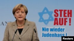 German Chancellor Angela Merkel, standing in front of a sign that reads "Stand up!" makes an address during an anti-Semitism demonstration at Berlin's Brandenburg Gate, Sept. 14, 2014. 