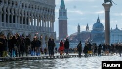 Orang-orang berjalan di Lapangan San Marko di Venesia Italia yang digenangi banjir hari Kamis (14/11). 