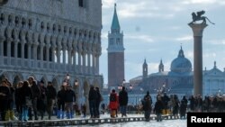 Para pejalan kaki melintasi jalan setapak darurat di Alun-alun St. Mark di Venesia, Italia, yang terdampak banjir, 14 November 2019.