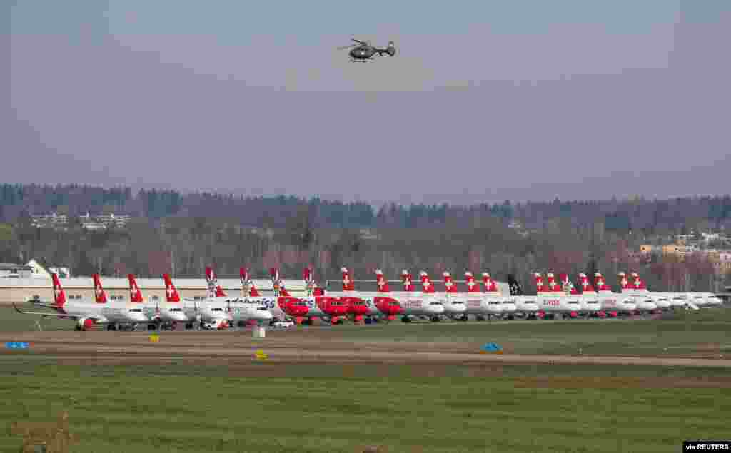 The Swiss Army Eurocopter EC635 flies above the aircrafts of Swiss Airlines, Edelweis Air and Helvetic Airways that are parked at an airbase in Duebendorf, Switzerland.