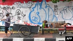 Seorang pemulung menarik gerobak sementara seorang pria tertidur di kursi, Jakarta, 21 April 2020. (Foto: AFP)