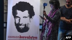 Seorang jurnalis berdiri di depan poster yang menampilkan filantropis Osman Kavala yang dipenjara, saat konferensi pers yang digelar oleh pengacaranya, di Istanbul, Turki, 31 Oktober 2018. (Foto: dok).