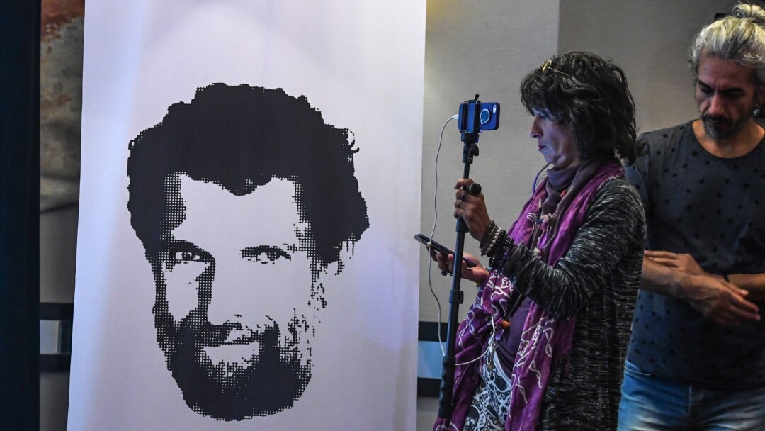 FILE - A journalist stands in front of a poster featuring jailed philanthropist Osman Kavala, during a press conference given by his lawyers, in Istanbul, Turkey, Oct. 31, 2018.