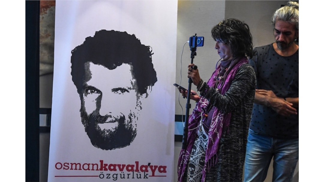 FILE - A journalist stands in front of a poster featuring jailed philanthropist Osman Kavala, during a press conference given by his lawyers, in Istanbul, Turkey, Oct. 31, 2018.