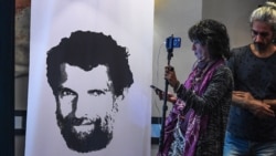 FILE - A journalist stands in front of a poster featuring jailed philanthropist Osman Kavala, during a press conference given by his lawyers, in Istanbul, Turkey, Oct. 31, 2018.