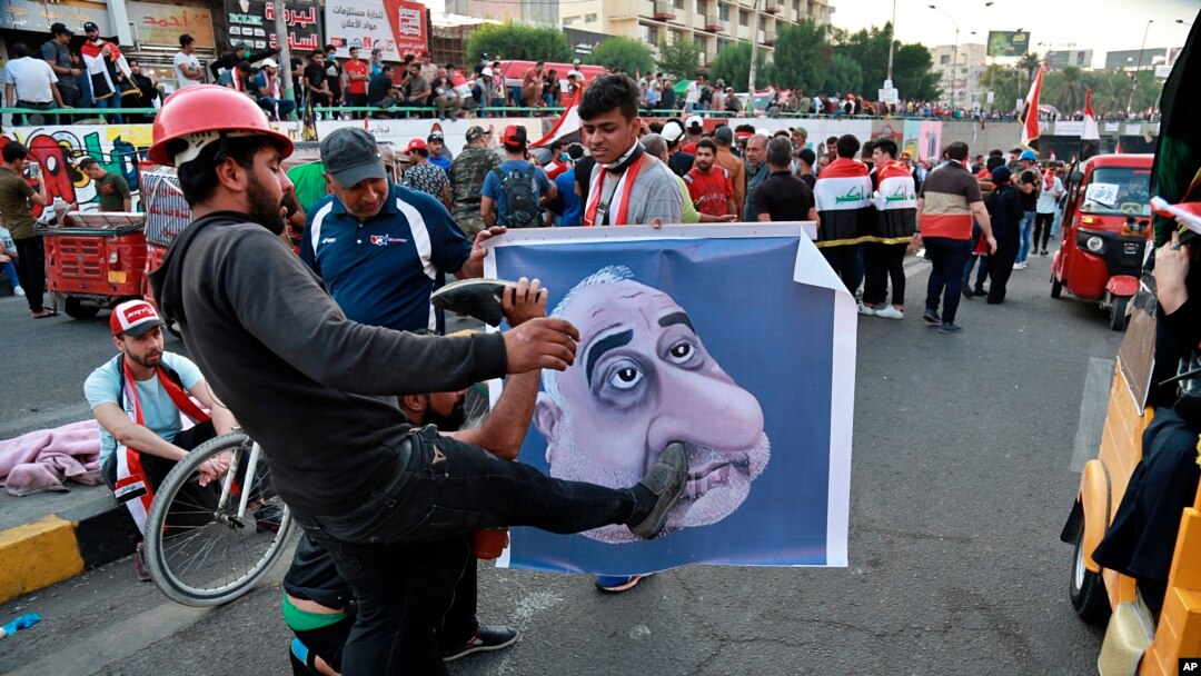 Protesters hit a poster showing Iraqi Prime Minister Adel Abdel-Mahdi with shoes during ongoing anti-government protests in Baghdad, Iraq, Nov. 3, 2019. 