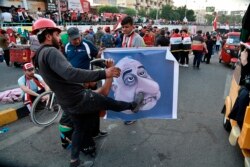 FILE - Protesters hit a poster showing Iraqi Prime Minister Adel Abdul Mehdi with shoes during ongoing anti-government protests in Baghdad, Iraq, Nov. 3, 2019.