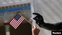 ARCHIVO - Una niña sostiene una bandera estadounidense junto a una escultura después de una ceremonia de naturalización en el Museo Metropolitano de Arte de Nueva York el 22 de julio de 2014.