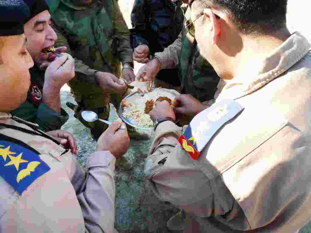 Petugas militer Irak berbagi makanan dalam satu piring, berisi daging dan nasi, untuk merayakan hari raya Syiah, Ashura (Sharon Behn/VOA).