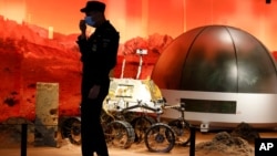 A security guard adjusts his mask near an exhibition of rovers and bio-domes on Mars in Beijing, July 23, 2020. 