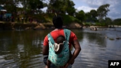 FILE - A migrant carrying a baby crosses the Chucunaque River after walking for five days in the Darien Gap, in Bajo Chiquito village, Darien province, Panama, Feb. 10, 2021.