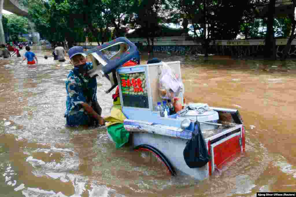 Seorang penjaja kaki lima mendorong gerobak makanannya melewati jalanan yang terendam banjir setelah hujan deras di Jakarta, Sabtu, 20 Februari 2021. (Foto: Ajeng Dinar Ulfiana / Reuters)