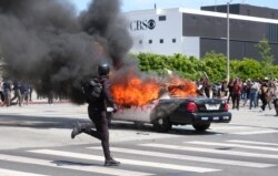 A person runs while a police vehicle is burning during a protest in Los Angeles, over the death of George Floyd, May 30, 2020.