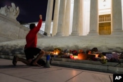 A man kneels in front of a memorial of candles and flowers outside the Supreme Court, Sept. 18, 2020, in Washington, after the Supreme Court announced that Justice Ruth Bader Ginsburg has died of metastatic pancreatic cancer.
