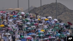 Peregrinos musulmanes usan sombrillas para protegerse del sol para arrojar piedras contra varias columnas en la lapidación simbólica del diablo, el último rito del haj anual, en Mina, cerca de la ciudad sagrada de La Meca, Arabia Saudí, el martes 18 de junio de 2024.
