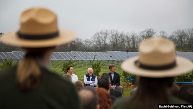 FILE - Former President Jimmy Carter, center, sits with his grandson Jason Carter, left, and George Mori, ｅxecutive vice president at SolAmerica Energy during a ceremony for a solar panel project on Jimmy Carter's farmland in Plains, Ga., Feb. 8, 2017.