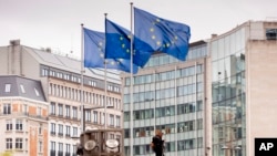FILE - European Union flags flap in the wind as two gardeners work outside EU headquarters in Brussels, Sept. 11, 2019.