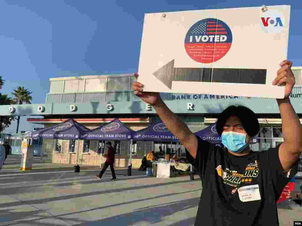 Un joven en el Dodger Stadium, usado como centro de votaci&#243;n cerca de Elysian Park en Los &#193;ngeles, sostiene un cartel previo al cierre del centro. noviembre 3 de 2020.