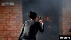 FILE - A women uses a cellphone to take pictures of a burning principal's school office in Mashau Dolly village in South Africa's northern Limpopo province, May 5, 2016. 