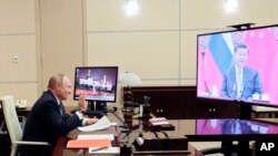 Russian President Vladimir Putin gestures during his videoconference with Chinese President Xi Jinping, right on the screen, in Moscow, Russia, Wednesday, Dec. 15, 2021. Russian President Vladimir Putin and Chinese leader Xi Jinping have held a video call