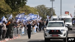 Israelis wave the national flag as the convoy of vehicles transporting the bodies of the four Israeli hostages handed over by Hamas, arrives at the entrance to the National Center of Forensic Medicine in Tel Aviv, Feb. 20, 2025.