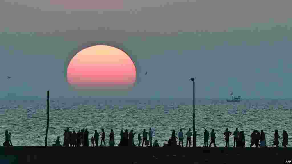 Orang-orang berjalan di sepanjang tepi laut saat matahari terbenam di dekat masjid Haji Ali di kota Mumbai, India,&nbsp;Senin sore 23 November 2020. (Foto: AFP)