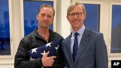 In this image provided by the U.S. State Department, Michael White holds an American flag as he poses for a photo on June 4, 2020 with U.S. special envoy for Iran Brian Hook in Zurich, Switzerland.