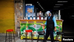 Un hombre desinfecta los asientos en el exterior de una venta de jugos naturales, tras la reapertura económica en San Salvador, El Salvador.