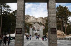 FILE - Visitors look at Mount Rushmore on March 22, 2019, in Keystone, S.D.