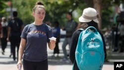 FILE - Georgina Maxwell, left, hands out coupons to pedestrians on the University of California at Berkeley campus in Berkeley, Calif., Thursday, July 18, 2019. (AP Photo/Jeff Chiu)