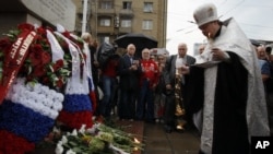 A Russian Orthodox priest prays as Moscovites light candles at a memorial to three men killed in the August 1991 hard line Communist coup attempt during a ceremony marking the 20th anniversary of the failure of the coup in downtown Moscow, Saturday, Aug. 