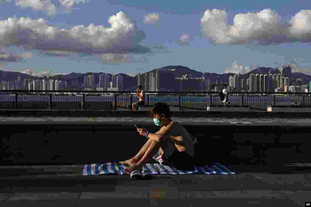 A man wearing a face mask to protect against the new coronavirus sits in the sun at a park in Hong Kong, Wednesday, July 22, 2020.