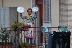 A resident uses pot lids to play cymbals as she takes part in a music flash mob called "Look out from the window, Rome mine!" The event sought to liven up the city's silence during the coronavirus lockdown, March 13, 2020.