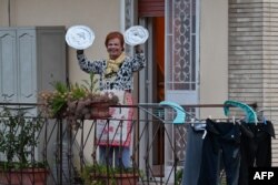 A resident uses pot lids to play cymbals as she takes part in a music flash mob called "Look out from the window, Rome mine!" The event sought to liven up the city's silence during the coronavirus lockdown, March 13, 2020.