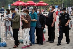 A security guard watches residents wearing face masks to help curb the spread of the coronavirus line up to receive the Sinopharm COVID-19 vaccine at a vaccination center in the Central Business District in Beijing, June 2, 2021.