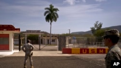 ARCHIVO - Un soldado del Ejército, der, y un miembro de la infantería de Marina permanecen frente a las verjas que separan el territorio cubano de la Base Naval estadounidense, el 6 de junio de 2018, en Bahía de Guantánamo, Cuba.