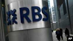 FILE - People walk past one of the headquarters buildings showing the logo of the Royal Bank of Scotland in London, Jan. 26, 2017.