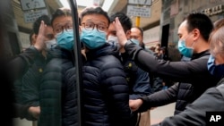 Redaktur Stand News Patrick Lam, tengah, dikawal polisi masuk ke dalam mobil van usai menggeledah barang bukti di kantornya di Hong Kong, Rabu, 29 Desember 2021. (Foto: AP)