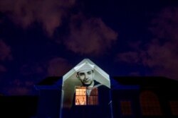An image of veteran Harry Malandrinos is projected onto the home of his son, Paul Malandrinos, as he looks out a window with his wife, Cheryl, in Wilbraham, Mass., May 16, 2020.