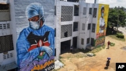 Residents in Mombassa, Kenya, walk in front of informational murals painted on the side of an apartment block about the coronavirus and paying tribute to medical workers with the messages "We'll Protect You" and "We Salute You," Aug. 17, 2020.