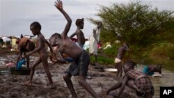 In this photo taken Thursday, June 5, 2014, displaced children wash themselves on the muddy bank of a river just outside the United Nations base which has become home to thousands of those displaced by recent fighting, in the town of Malakal, Upper Nile State, South Sudan. 