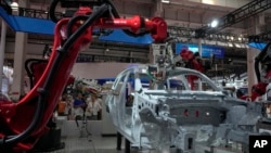 FILE - Visitors look on as robotic arms assemble a vehicle frame in Beijing on Aug. 17, 2023. Factory activity in China grew for the first time in six months in September.