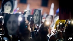 FILE - In this Nov. 29, 2019 file photo, people hold pictures of slain journalist Daphne Caruana Galizia as they protest outside the office of the Maltese Prime Minister Joseph Muscat, in Valletta, Malta. 