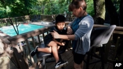 FILE - Holly Sewell helps Byron Xol, 9, an immigrant from Guatemala, talk to his family by phone, June 24, 2019, in Buda, Texas.