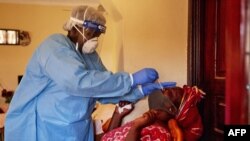 FILE - A member of South Sudanese Ministry of Health Rapid Response Team takes a nasal sample from a woman at her home after she came into into contact with a confirmed COVID-19 case, in Juba, South Sudan, April 14, 2020.