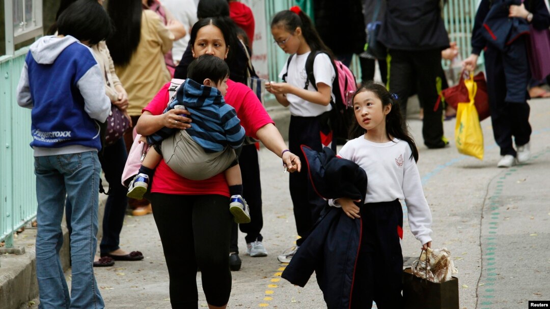 Seorang pembantu rumah tangga asing menggendong seorang anak dan menggandeng anak lainnya di luar sebuah sekolah di Hong Kong, 26 February 2013.(REUTERS/Bobby Yip). Seorang PRT Filipina berjuang untuk memperoleh ijin menetap di Hong Kong dengan mengajukan argumentasi ke Mahkamah Agung Tertinngi wilayah itu, Selasa (26/1).
