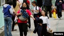 Seorang pembantu rumah tangga asing menggendong seorang anak dan menggandeng anak lainnya di luar sebuah sekolah di Hong Kong, 26 February 2013.(REUTERS/Bobby Yip). Seorang PRT Filipina berjuang untuk memperoleh ijin menetap di Hong Kong dengan mengajukan argumentasi ke Mahkamah Agung Tertinngi wilayah itu, Selasa (26/1).